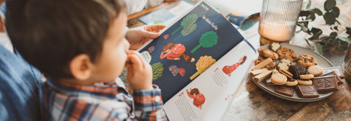Adventszeit Junge isst Plätzchen und liest gemeinsam mit seiner Mutter in einer Zeitschrift Adventszeit Junge isst Plätzchen und liest gemeinsam mit seiner Mutter in einer Zeitschrift